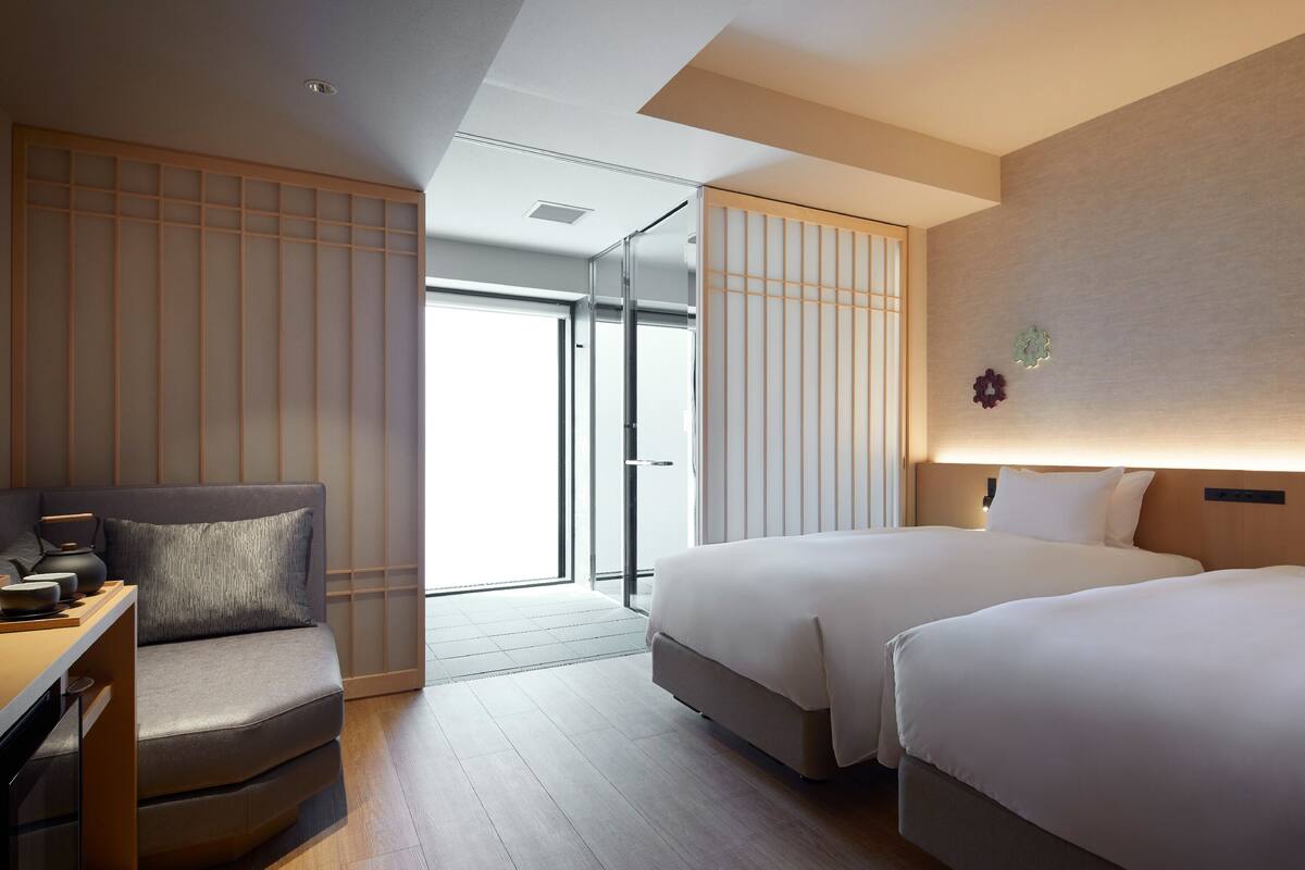 Een moderne hotelkamer met een bank, twee bedden, een bureau en een schuifdeur naar een balkon.