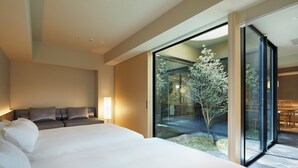 Une chambre d’hôtel moderne avec un grand lit, un canapé et une porte vitrée donnant sur un jardin.