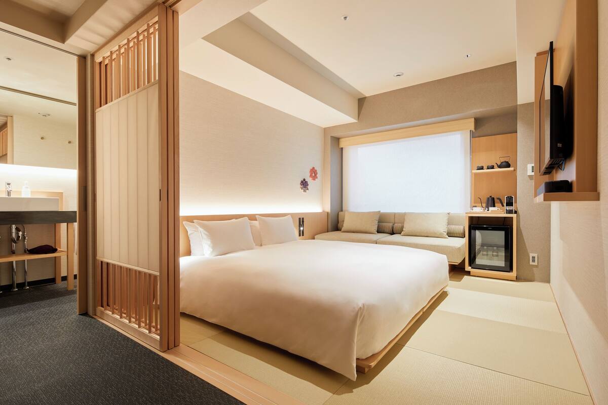 Een moderne hotelkamer met een groot bed, een slaapbank, een kleine televisie en een kitchenette.