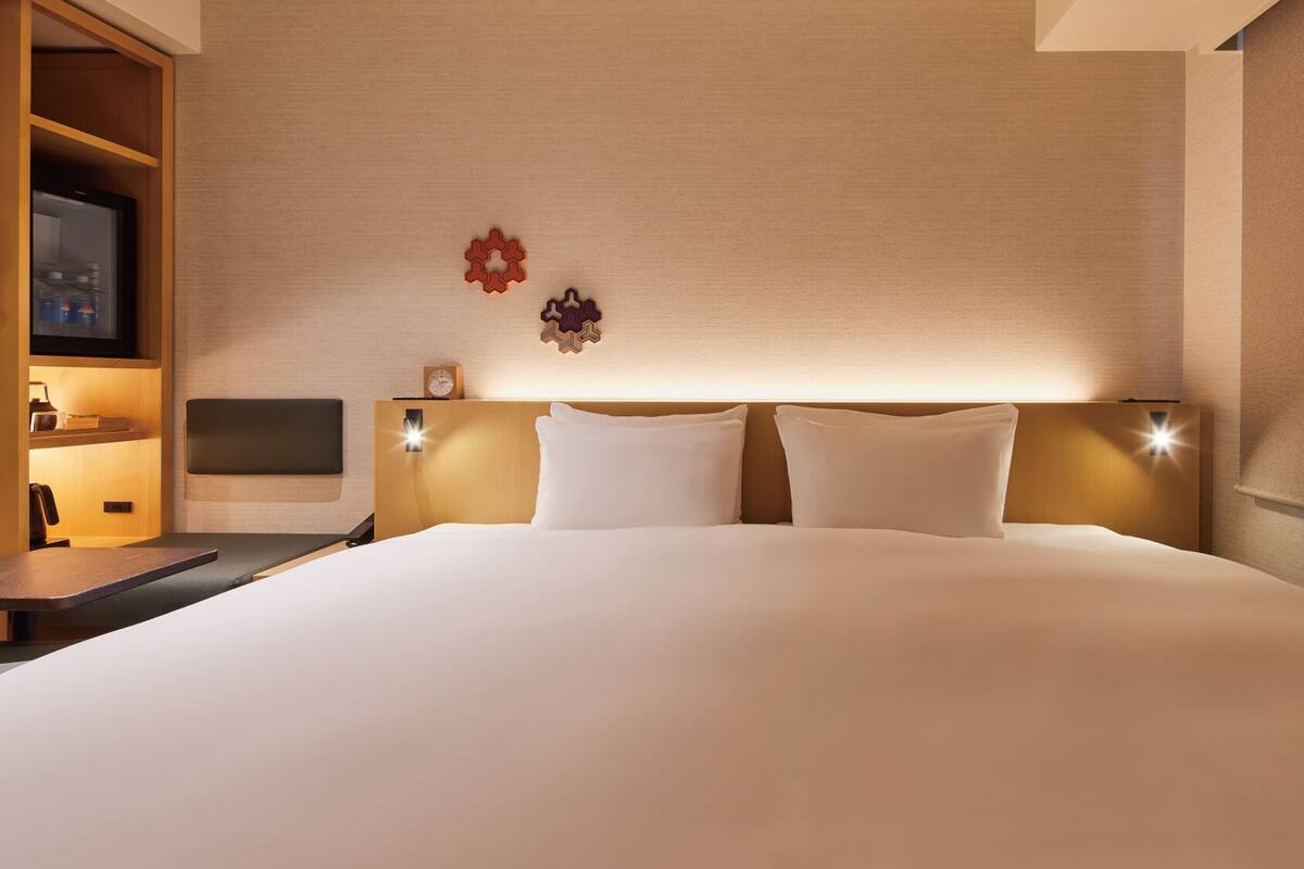 Une chambre d’hôtel avec un grand lit, des tables de chevet, une télévision et des lampes fixées au mur.