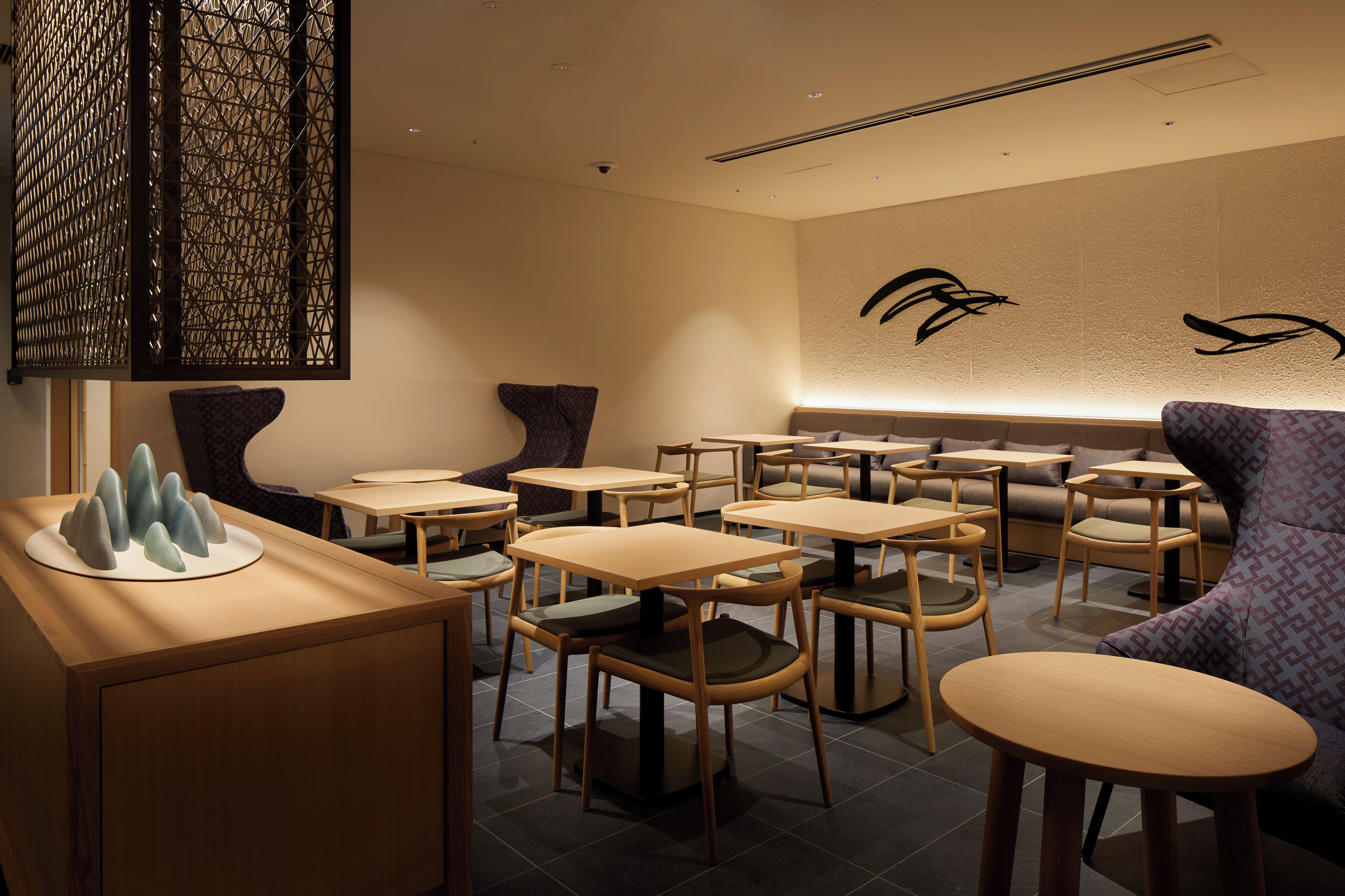 Ein modernes Restaurant-Interieur mit mehreren Tischen und Stühlen, einem Wandkunstwerk und einer Sitzecke mit gepolstertem Sofa.