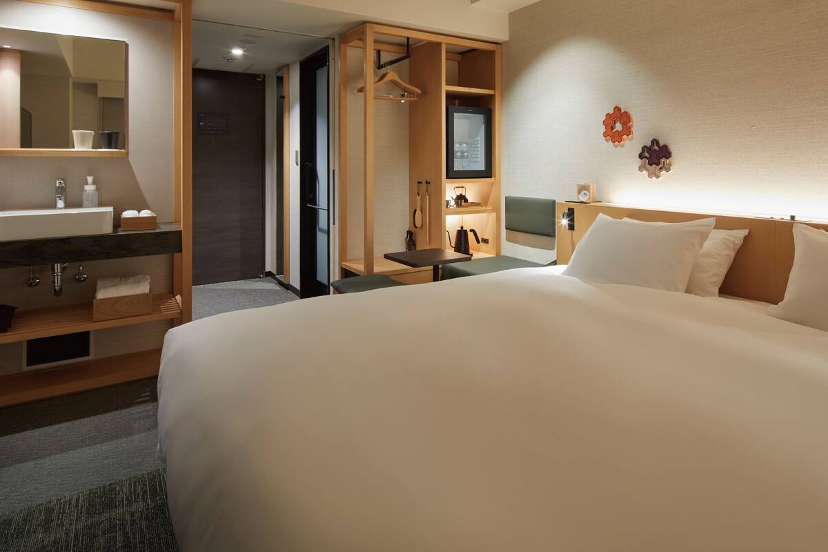 Une chambre d’hôtel avec un grand lit, une salle de bain avec un lavabo et un miroir, une télévision et une armoire.