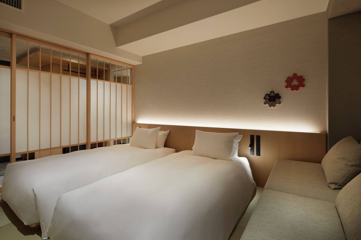 Een hotelkamer met twee bedden, een bank, een schuifdeur en decoratieve wandelementen.