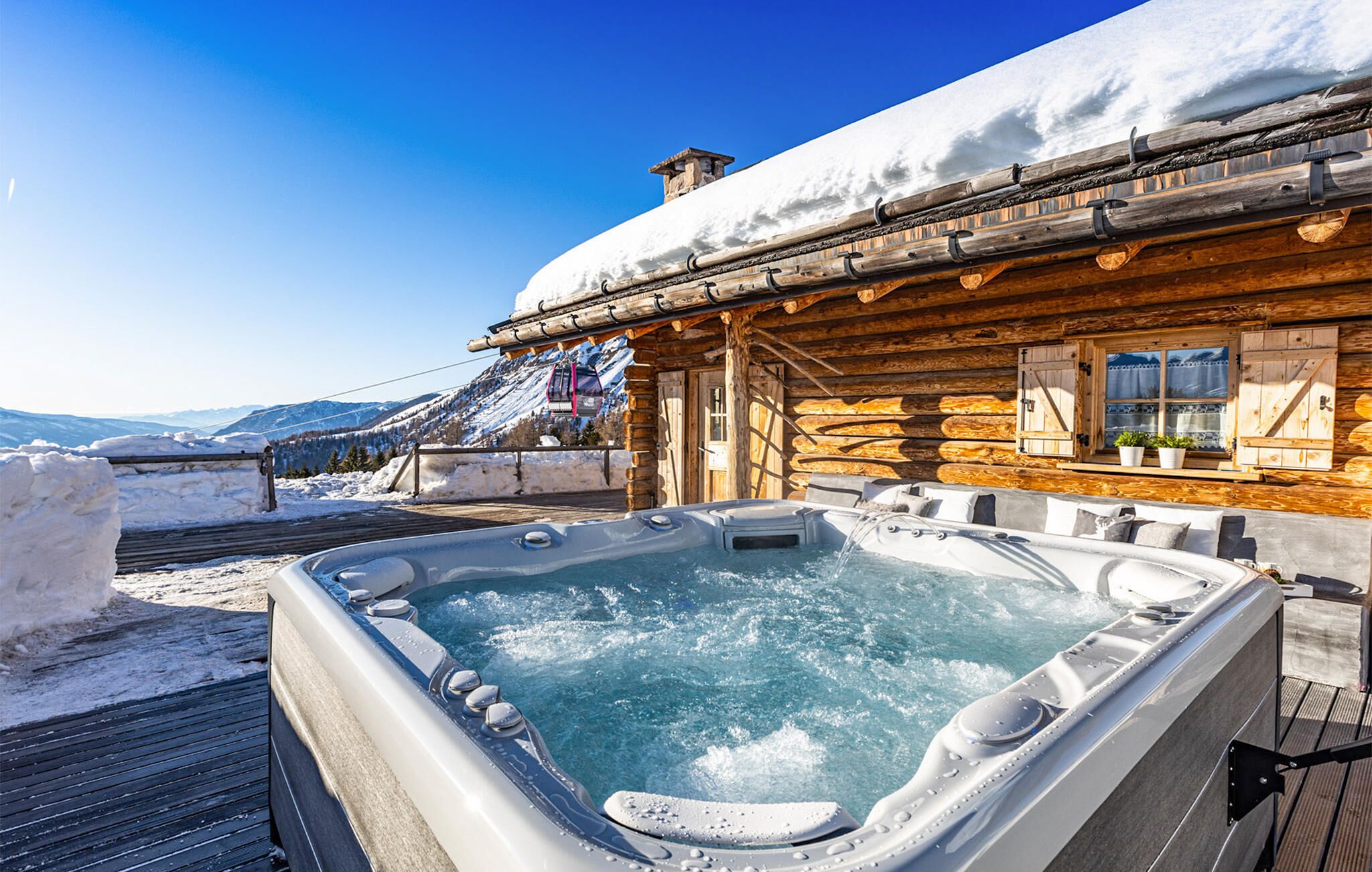 Une cabane en bois avec un jacuzzi et une montagne enneigée en toile de fond.