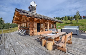 Ein rustikales Blockhaus mit einer Holzdiele, Sitzgelegenheiten im Freien und Grillplatz.