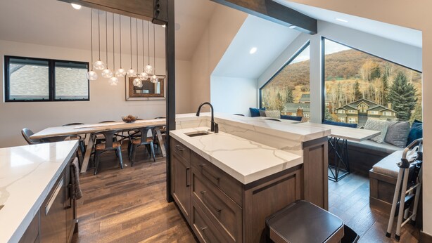 A modern kitchen with a large island, wooden flooring, and a view of a mountainous landscape through large windows. - DV Loop Old Town Home by Luxury Mountain Destinations (Park City)