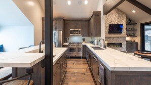 A modern kitchen with a central island, stainless steel appliances, and a stone accent wall. - DV Loop Old Town Home by Luxury Mountain Destinations (Park City)