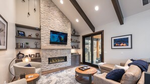 A modern living room with a stone fireplace, comfortable seating, and a flat-screen TV mounted on the wall. - DV Loop Old Town Home by Luxury Mountain Destinations (Park City)