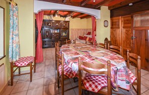 A dining area with a large table covered in a patterned tablecloth, surrounded by wooden chairs.