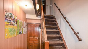 Eine Holztreppe mit Metallgeländer, eine Holztür und verschiedene Informationsplakate an der Wand.