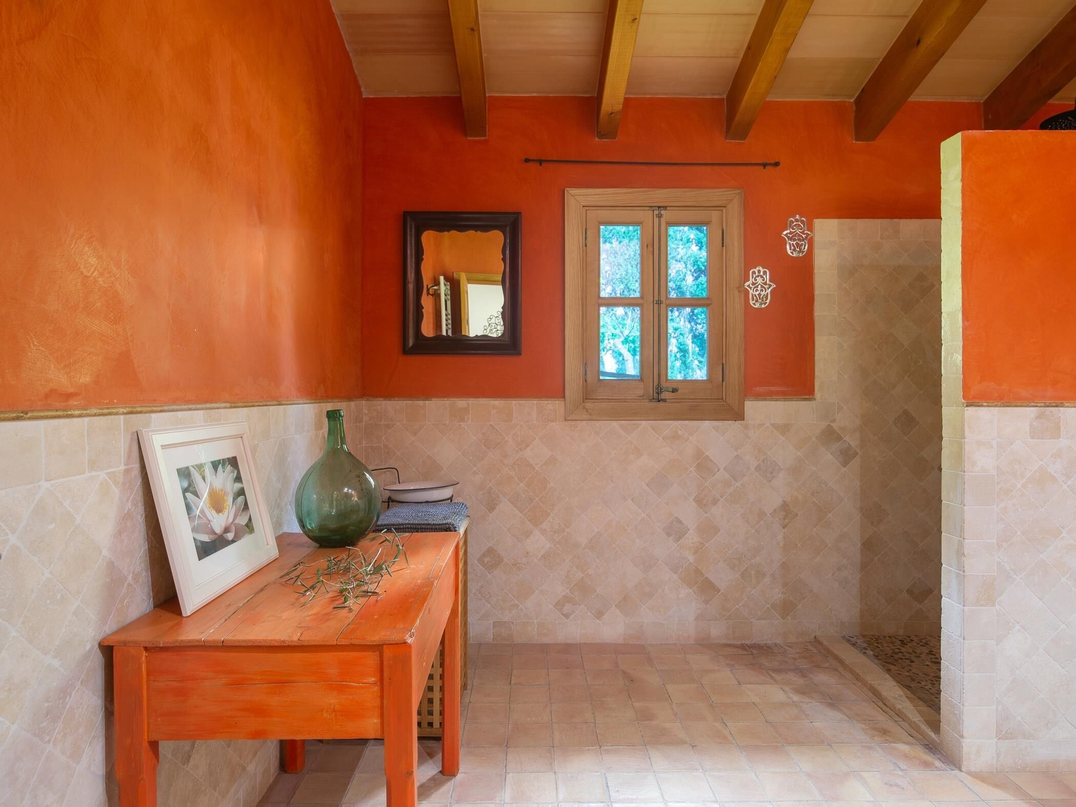 A bathroom with orange walls, a wooden ceiling, a window, a mirror, and a tiled floor.