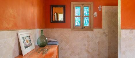A bathroom with orange walls, a wooden ceiling, a window, a mirror, and a tiled floor.