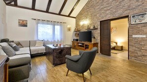 Una sala de estar acogedora con sofá, sillón y una mesa de centro, un televisor de pantalla plana sobre un mueble de madera, y una pared de piedra.