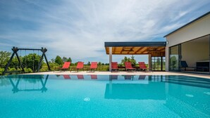 Una piscina con sillas de descanso rojas y una pérgola de madera.