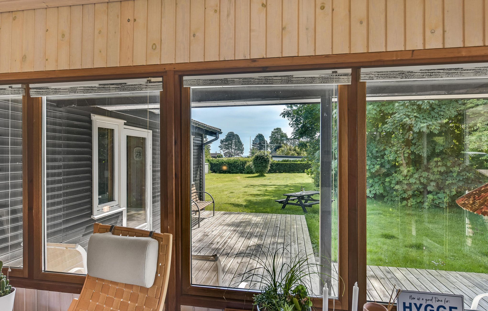 Ein Zimmer mit großem Fenster mit Blick auf eine Holzterrasse und einen Rasen.