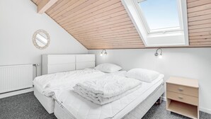 A bedroom with a sloped ceiling, a skylight, a bed with white bedding, a bedside table, and a wall-mounted mirror.