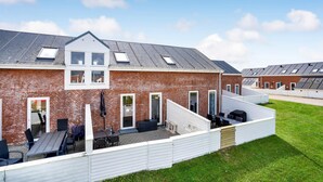 A brick building with a sloped roof, a covered patio with outdoor seating, and a small garden area.