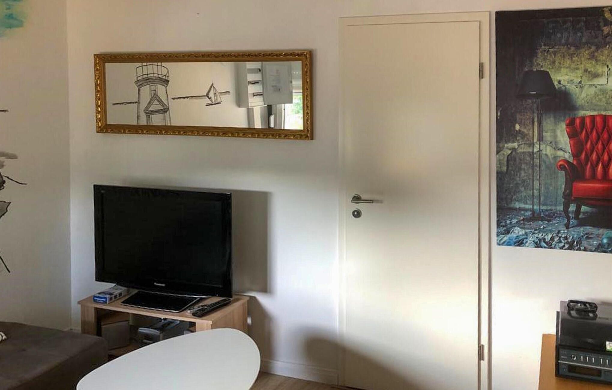 A room with a television on a stand, a door, and a framed picture on the wall.