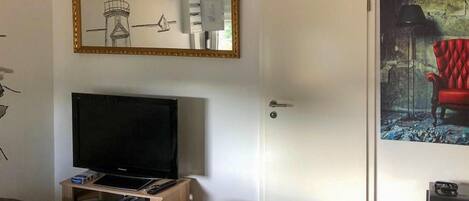 A room with a television on a stand, a door, and a framed picture on the wall.