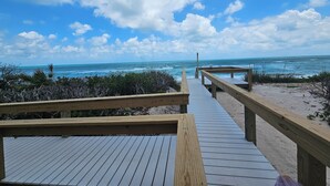 Une promenade en bois menant à la plage, d’où l’on a une vue dégagée sur l’océan et le ciel.