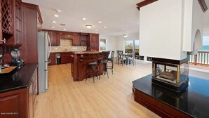 Une cuisine spacieuse avec des meubles de rangement en bois, un îlot central doté de tabourets et une cheminée.