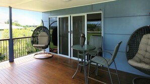 A balcony with a wooden floor, a glass door, and two chairs. - 24 Lihs Street Elliott Heads (ELLIOTT HEADS)