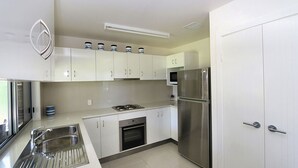 A modern kitchen with white cabinets, stainless steel appliances, and a built-in oven. - 24 Lihs Street Elliott Heads (ELLIOTT HEADS)