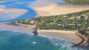 An aerial view of a coastal area with a sandy beach, a small settlement with houses, and a rocky shoreline. - 24 Lihs Street Elliott Heads (ELLIOTT HEADS)