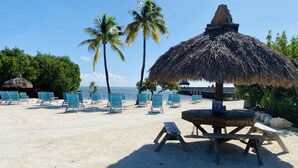 A beach with thatched umbrellas, lounge chairs, and a wooden table. - 2BR - Key Largo Sunshine Getaway (Tavernier)