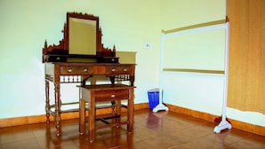 A room with a wooden desk, a mirror, a chair, a broom, and a whiteboard.