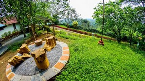 A garden with a circular stone structure surrounded by grass, a wooden bench, and a pergola.