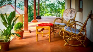 A wooden table with a red cloth, a wicker chair with a checkered cushion, and potted plants on a patio. - Standard Double Room-wayanad (Vythiri)