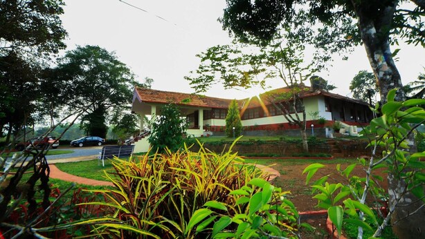 A two-story house with a tiled roof, surrounded by lush greenery and a paved driveway. - Bungalow With Tea Garden View (Vythiri)