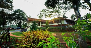 A two-story house with a tiled roof, surrounded by lush greenery and a paved driveway. - Bungalow With Tea Garden View (Vythiri)