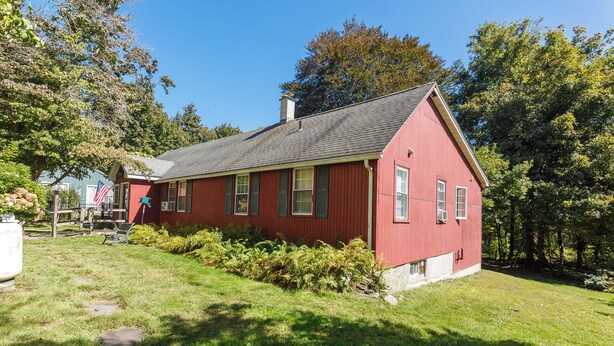Een rode woning met een schuin dak, omringd door groen en bomen.