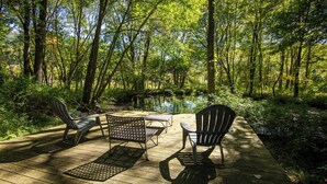Een houten terras met tuinmeubilair, omringd door bebossing en een klein waterlichaam.