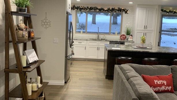 A modern kitchen with white cabinets, a wooden island, and a view of a snowy landscape through large windows. - Golf Course Villa (East Wenatchee)