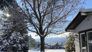 A snow-covered outdoor seating area with a tree and a building in the background. - Golf Course Villa (East Wenatchee)