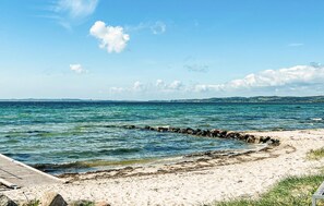 Ein Strand mit klarem Wasser, einer Holzstege und weiter Küste im Hintergrund.