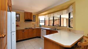 A kitchen with wooden cabinets, a white refrigerator, a dishwasher, a sink, and a window with blinds. - 36 Trevors Road Bargara (Bargara)