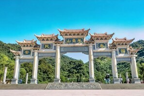 Um arco chinês tradicional com inscrições, com colinas verdes exuberantes ao fundo.