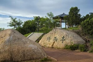 Un chemin de pierres menant à un pavillon orné de caractères chinois, entouré de grands rochers et de verdure.