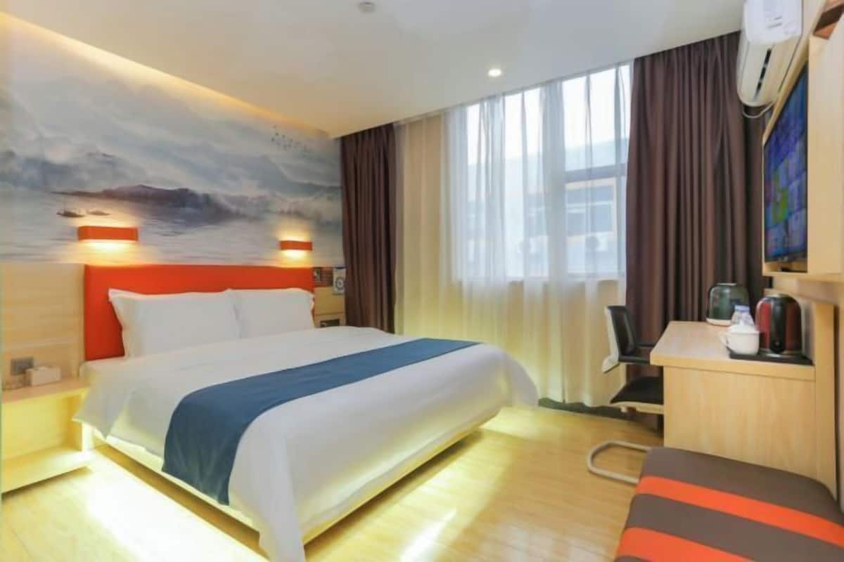 A hotel room with a bed, a desk, a chair, a coffee maker, and a painting on the wall.