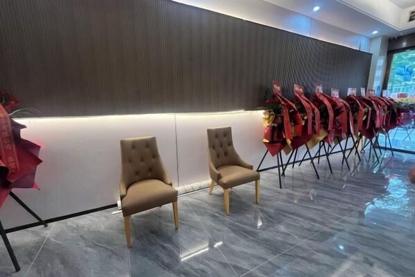 Un hall d’hôtel avec une rangée de fauteuils beiges, un mur foncé à texture marquée et un sol carrelé.