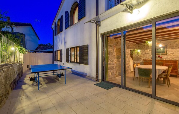 A courtyard with a ping pong table, a dining area with a round table and chairs, and a stone wall. - Stunning home in Ruzici (Ruzici)