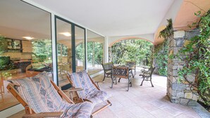 Une terrasse ensoleillée avec un mur en pierre, une table à manger avec des chaises et un canapé agrémenté de coussins à motifs.