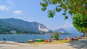 Une plage au bord d’un lac, avec des bateaux, des gens et des montagnes en arrière-plan.