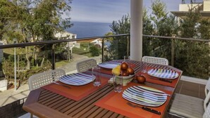 Una mesa de comedor en un balcón con vistas al mar y vegetación circundante.