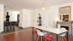 A modern kitchen with a central island, a dining area with a marble table and chairs, and a fireplace with a mirror above it. - Suite Napoléon III - 6.pers - downtown Charleville-Mézières (Charleville-Mézières)
