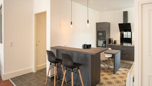 A modern kitchen with a central island, bar stools, a coffee machine, and a built-in oven. - Suite Napoléon III - 6.pers - downtown Charleville-Mézières (Charleville-Mézières)